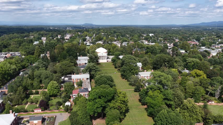 Red brick pavilions and garden walls border the UVA Lawn in Charlottesville, Virginia, with shaded walkways leading toward the distant Rotunda. Aerial drone wide shot