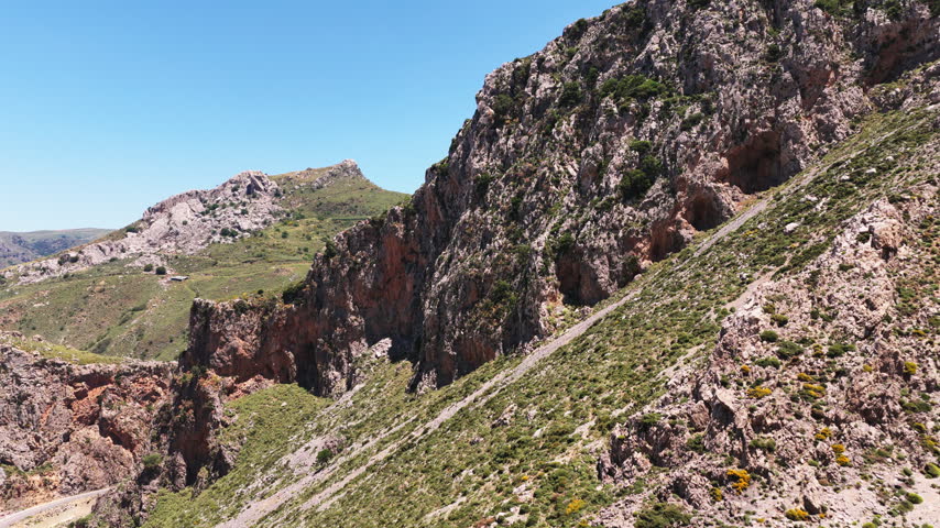 Aerial drone view of a rocky gorge opening onto a green valley with mountains beyond, Kourtaliotiko Gorge, Greece