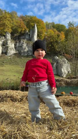 Young boy plays with a large orange pumpkin while sitting in hay at a farm.
