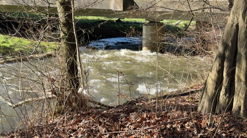 Rushing murky water flowing rapidly under a concrete bridge after heavy rainfall in the woods