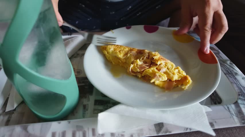 Close-up view of a person eating a freshly made omelette with ham for breakfast on a tray