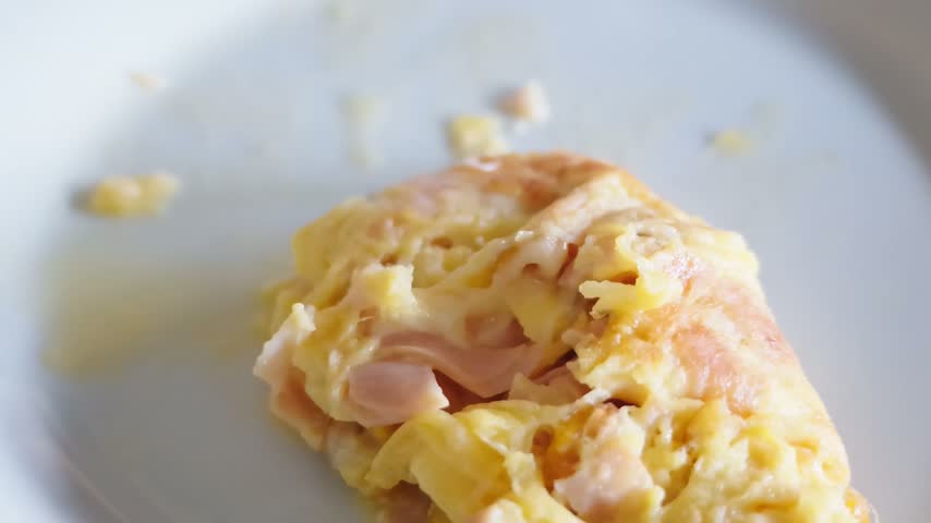 Close-up view of a fork cutting a freshly cooked omelette with ham and melted cheese