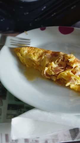 Close-up view of a person eating a freshly made omelette with ham for breakfast on a tray
