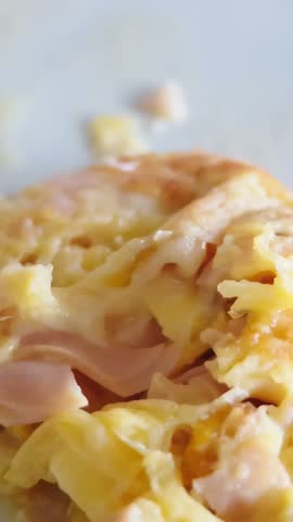 Close-up view of a fork cutting a freshly cooked omelette with ham and melted cheese