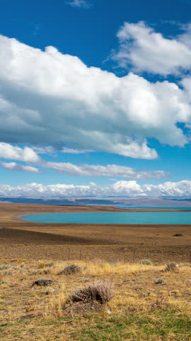 Scenic landscape of a turquoise lake in the Patagonia region of Argentina with dry grass fields and a blue sky with clouds