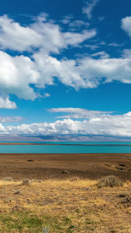 Scenic landscape of a turquoise glacial lake in Patagonia with dry golden grass in the foreground and mountains under a blue sky with clouds