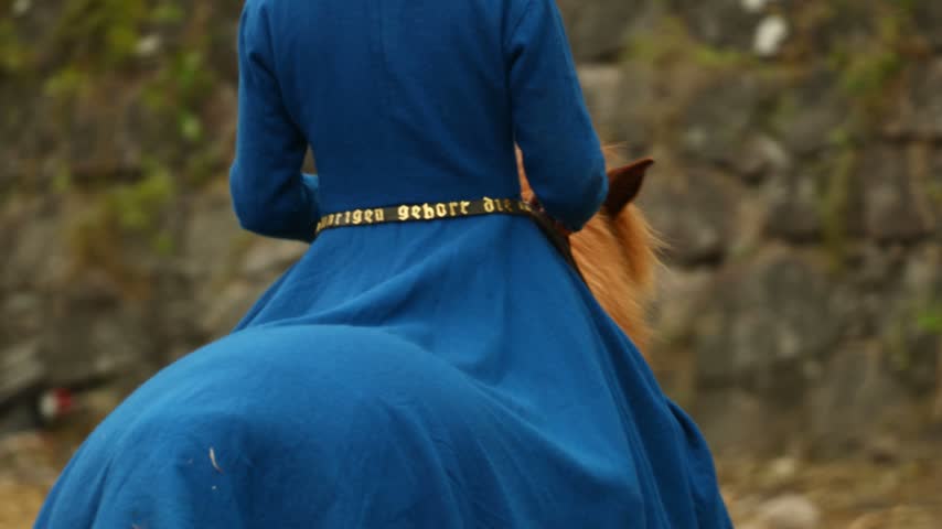 A woman in a blue dress rides a brown horse.