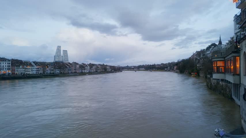 Point of view walking on bridge looking out over wide Rhine River and historic city skyline at dusk in Basel, Switzerland