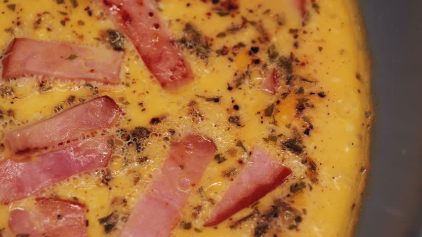 Omelette with bacon and spices frying in a pan, close-up cooking process.