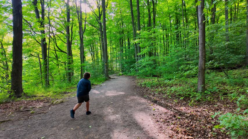 Young boy hiking on a trail in a lush green forest at Rattlesnake Point Conservation Area in Milton, Ontario