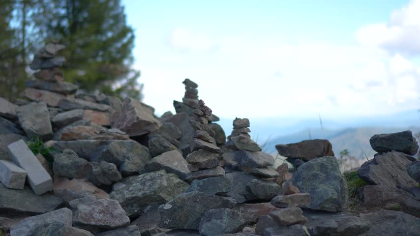 Close up of balanced stone pyramids on a mountain peak with a slow camera push in and focus pull revealing a vast alpine valley