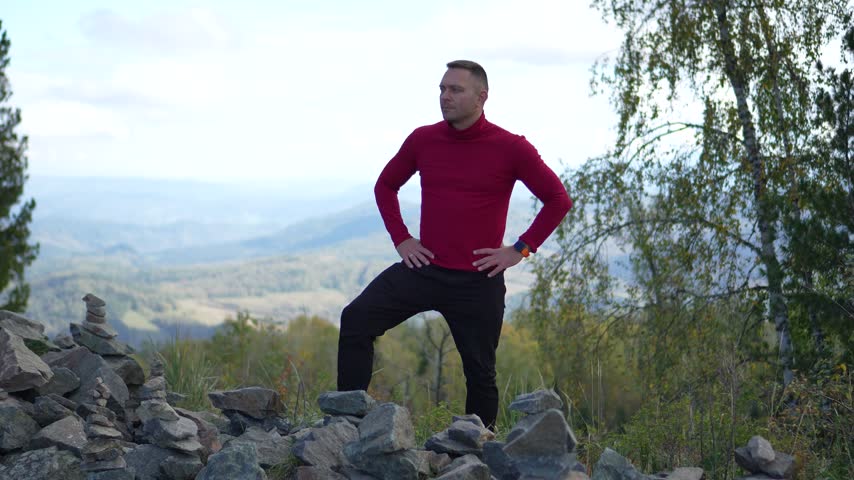 Handsome confident man standing with arms crossed on a mountain top with a slow camera push in