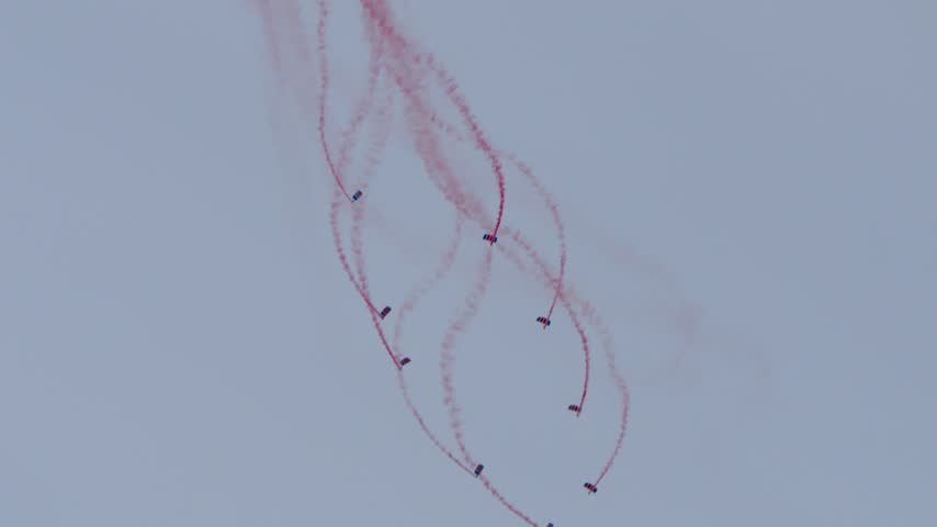 Parachute team floating to the ground with red smoke trails