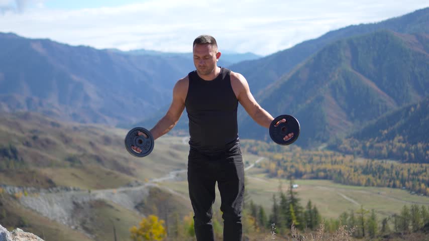 Athletic man holding weight plates out to the sides on a mountain pass with a static camera shot.
