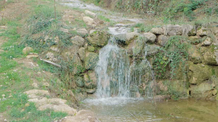 Small Natural Waterfall Cascading Over Rustic Stone Wall in Serene Rural Landscape