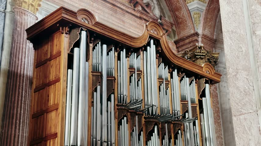 Close-up of church pipe organ with wooden carved case and metal pipes. Historic musical instrument inside Roman church interior.