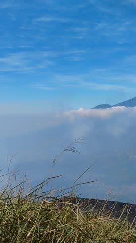 Scenic landscape of majestic mountain peak surrounded by sea of clouds under bright blue sky, Java, Indonesia