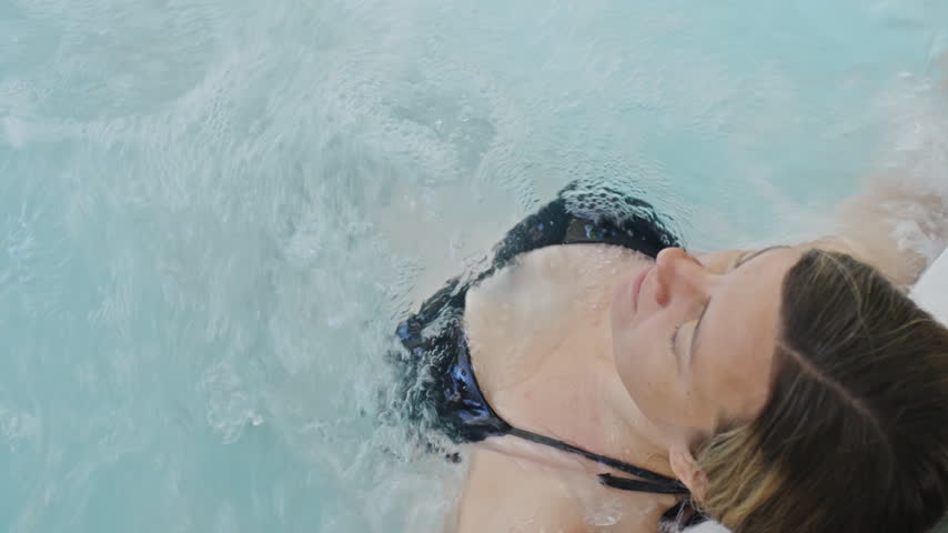 Woman in black swimsuit relaxing in bubbling water. Female enjoying a bubble massage in an inflatable hot tub. Wellness and home spa concept