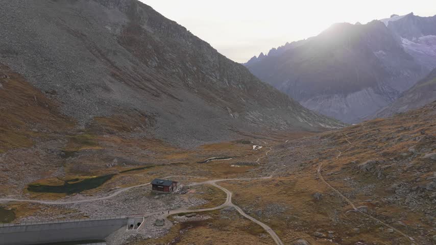 Aerial view of Aletsch Glacier with a small mountain hut and winding trails in the rocky landscape of Fieschertal, Valais, Switzerland.
