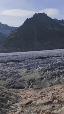 Aerial view of Aletsch Glacier with its vast ice field and rugged mountain peaks under lenticular clouds in Fieschertal, Valais, Switzerland.