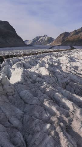 Aerial view of the vast Aletsch Glacier with its deep crevasses and surrounding mountain peaks in Fieschertal, Valais, Switzerland.