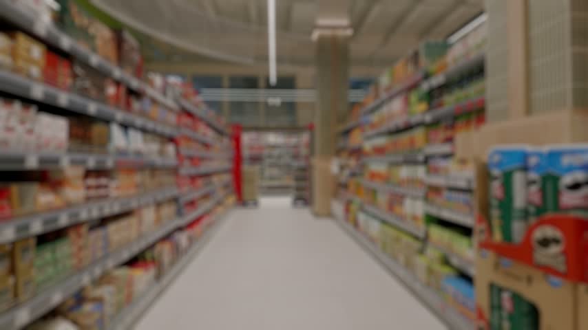 Empty supermarket aisle with shelves full of products. Point of view walking through a grocery store looking for food, an ideal background with a blurred, out-of-focus bokeh effect