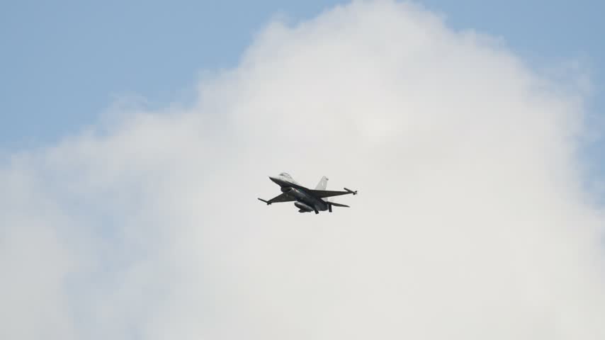 Powerful F16 Fighting Falcon military aircraft performing a low pass flight. The jet fighter is maneuvering against a blue sky with clouds