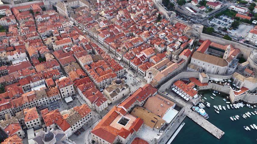 Aerial view of Dubrovnik, Croatia, at sunset, showcasing the historic coastal city, illuminated streets, Adriatic coastline and dramatic mountains surrounding the urban landscape.