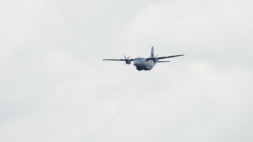 Powerful Alenia C 27J Spartan military transport aircraft with propellers spinning, flying against a cloudy sky during an airshow display