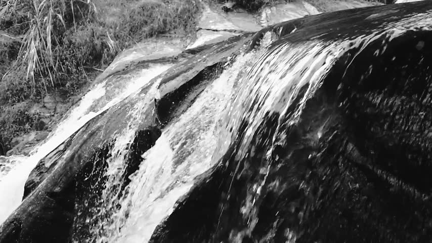 Black and white close up of water cascading smoothly over dark rocks in river