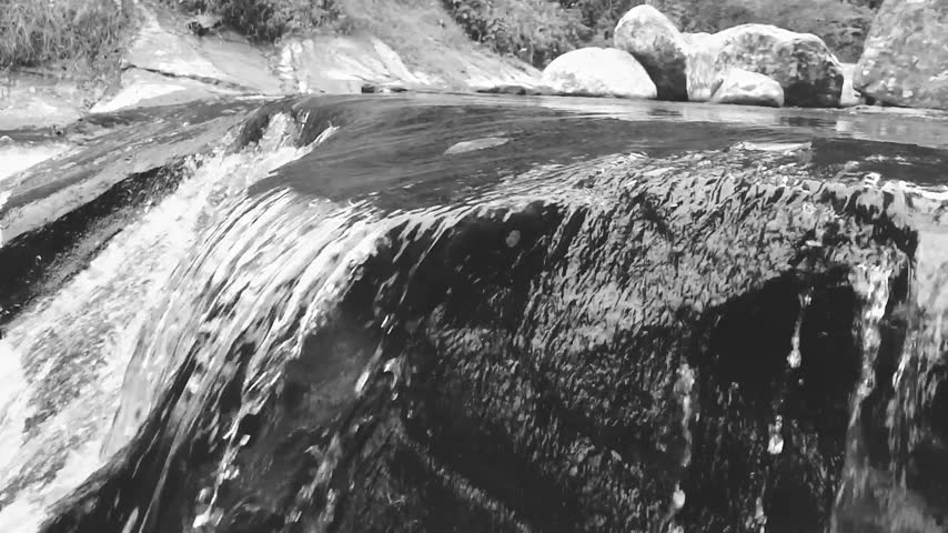 Black and white close up of water cascading smoothly over dark rocks in river