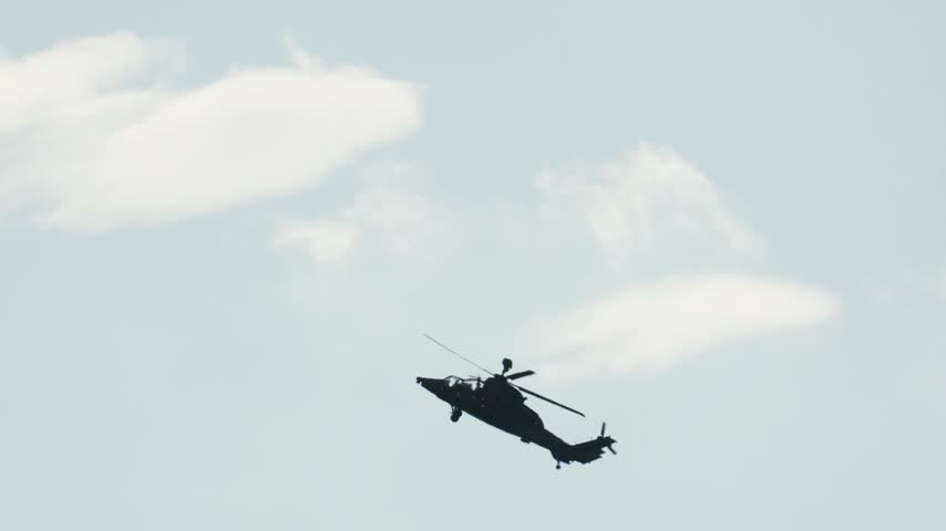 Military combat helicopter flying a mission against a cloudy sky. The gunship aircraft is silhouetted by the sun during an attack patrol