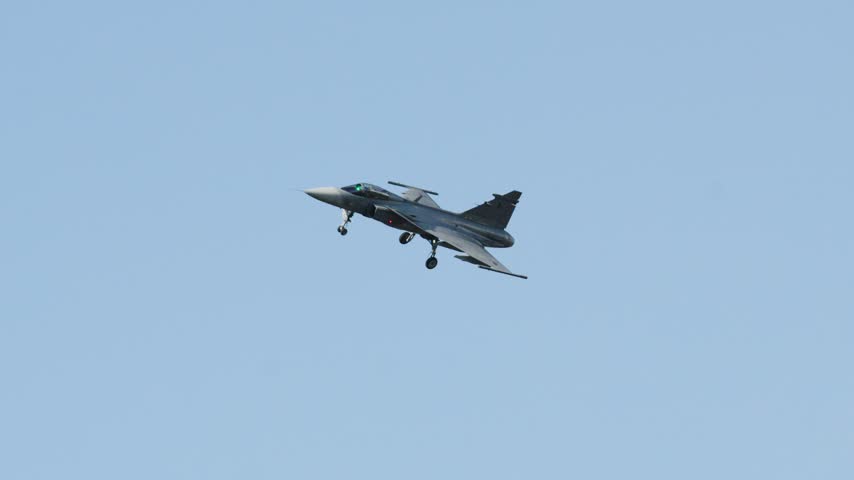Military Saab JAS 39 Gripen fighter jet preparing for landing. The multirole combat aircraft is flying with its landing gear down