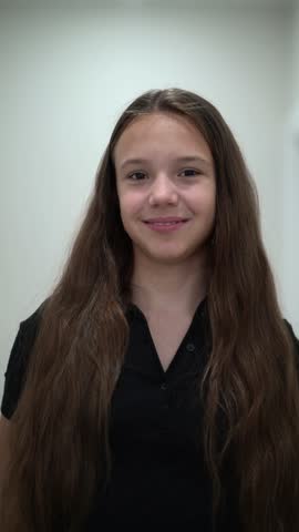 Portrait of smiling young girl with long brown hair in black shirt on white background.