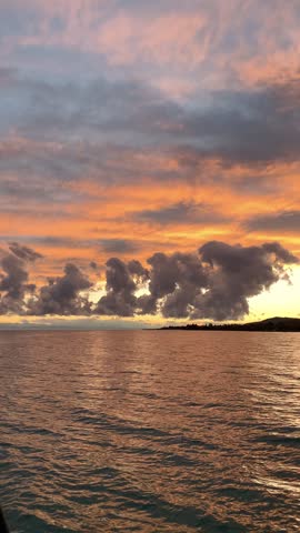 Vibrant orange sunset sky with dramatic clouds over rippling lake water and distant shoreline