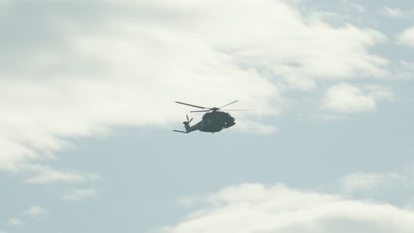 Military transport helicopter performing a challenging aerobatic loop maneuver against a cloudy sky during an airshow demonstration