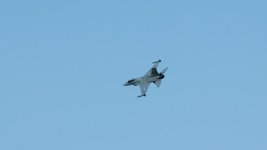Powerful military fighter jet performing aerial maneuvers in a cloudy blue sky. A single F 16 combat aircraft flying fast during a training exercise