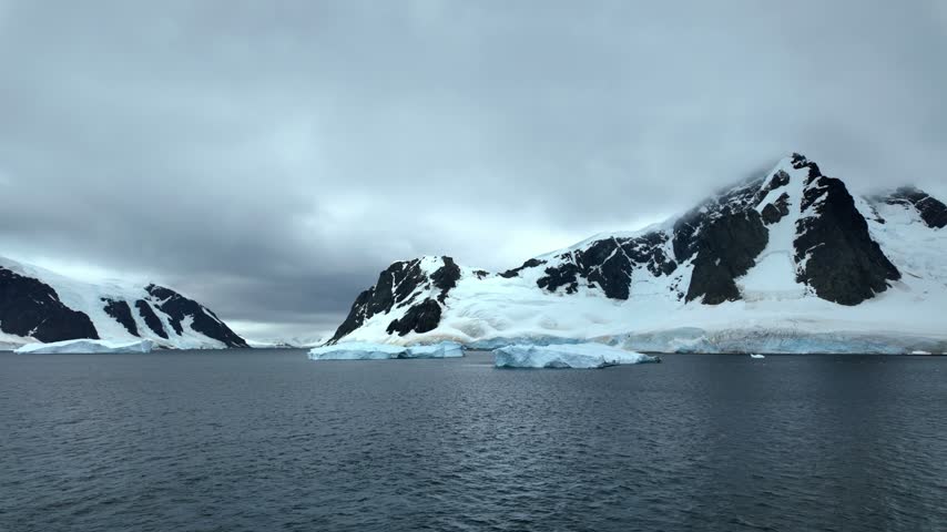 A sharp triangular mountain with exposed black rock towers over floating ice and dark Antarctic water in Antarctica.