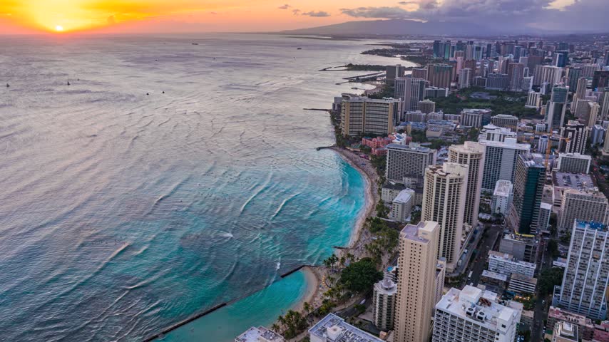 Aerial view of Waikiki Beach skyline at sunset with golden light reflecting on the ocean and high-rise buildings in Honolulu, Hawaii, United States.