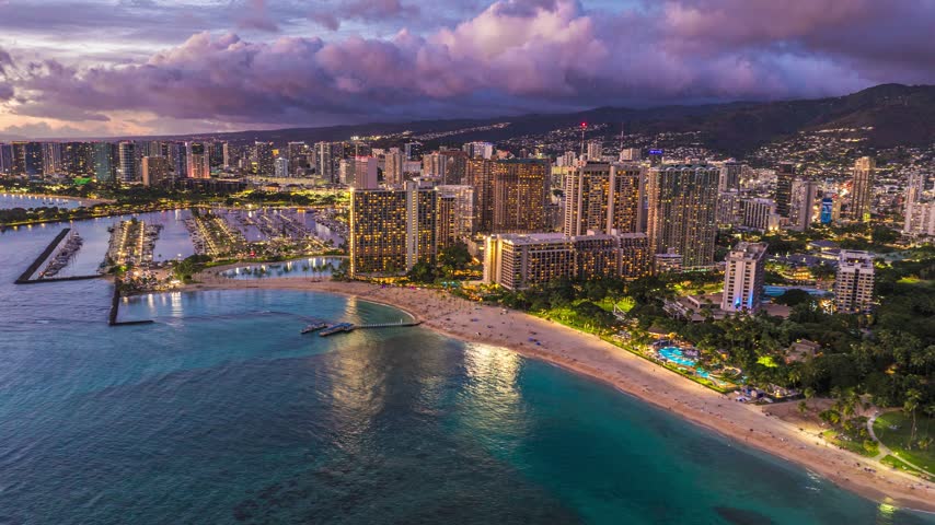 Aerial view of Honolulu skyline and Waikiki beach with illuminated hotels, boats in the marina, and sandy coastline in Honolulu, Hawaii, United States.
