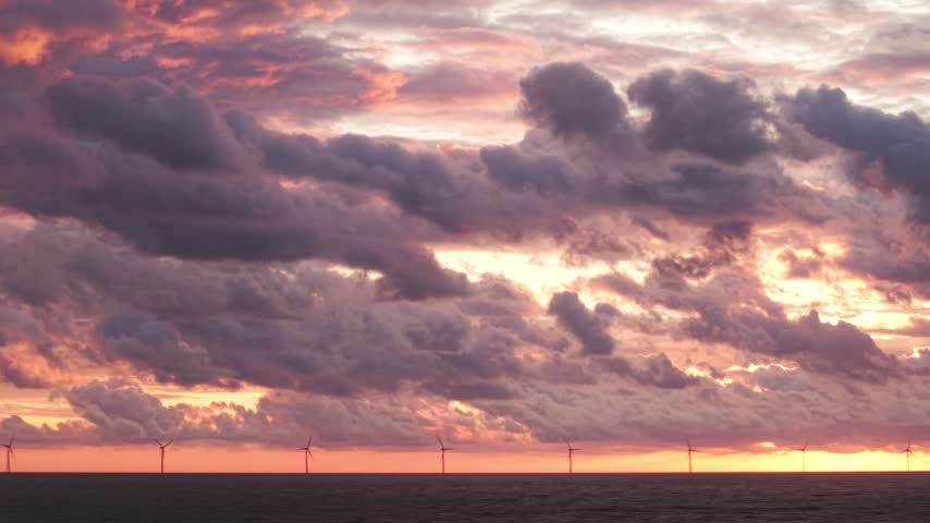 Aerial view of offshore wind farm with silhouettes of turbines against a dramatic purple and orange sunset sky over the North Sea near Hvide Sande, Denmark.