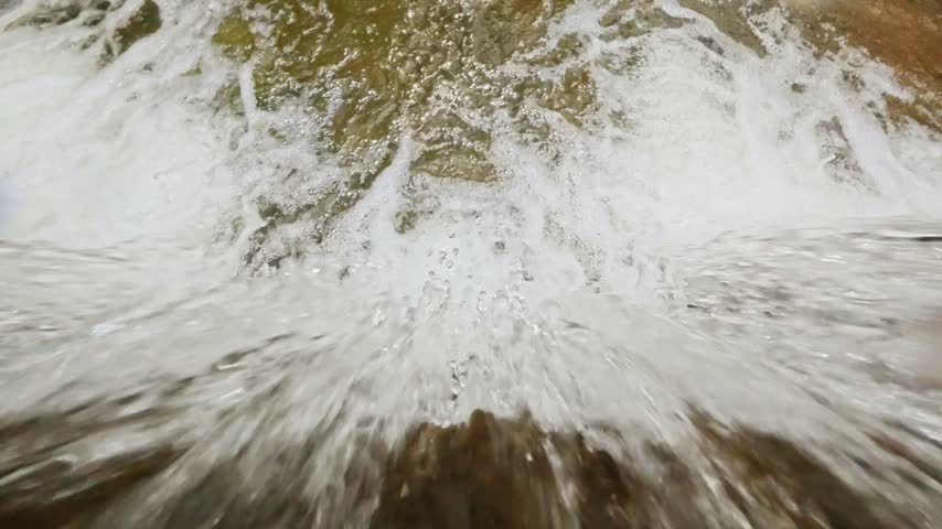 Close up top down view of fast flowing water rushing over a small waterfall creating white foam and splash

