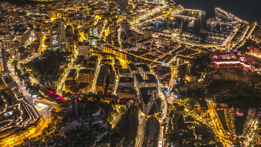 Aerial view of the illuminated cityscape of Monaco at night, featuring the harbor, dense urban architecture, and glowing coastal streets in Monaco, Monaco.