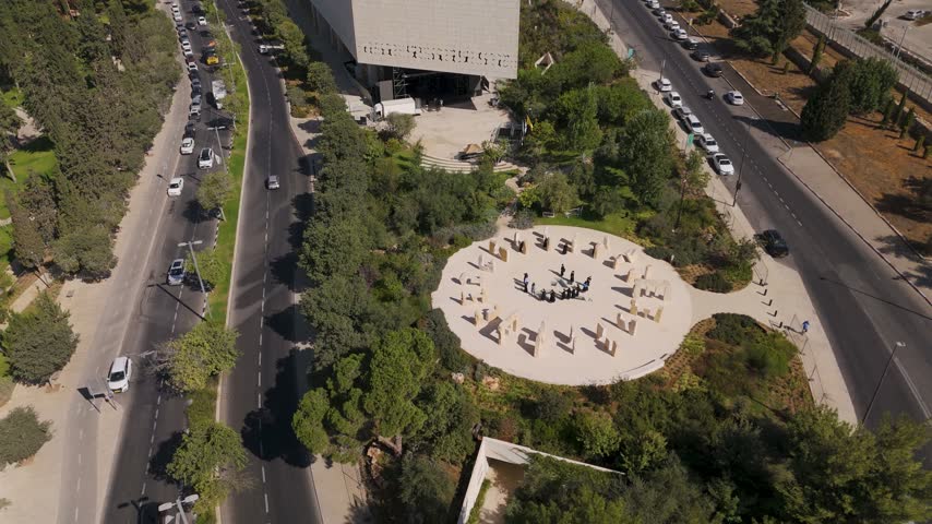 Aerial view of the National Library of Israel in Jerusalem, featuring a circular plaza with people, surrounded by lush trees and nearby roads in Jerusalem, Jerusalem District, Israel.