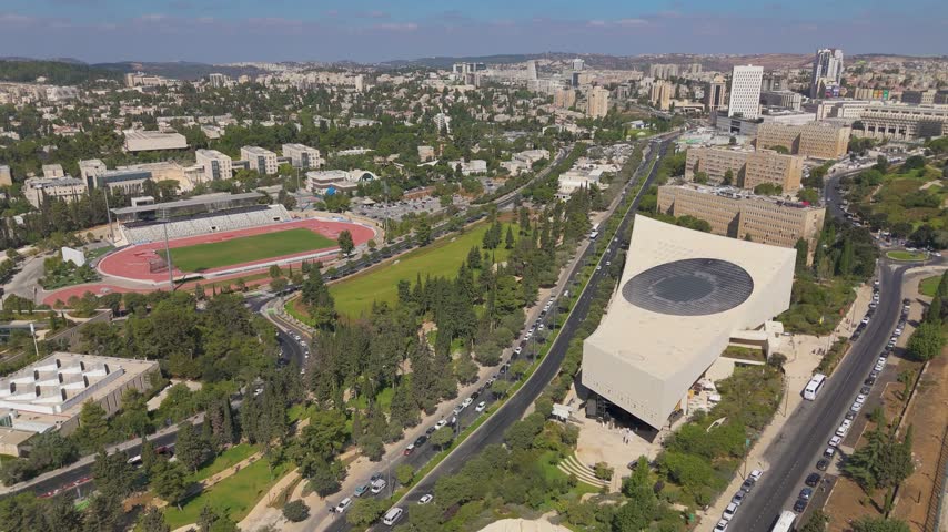 Aerial view of the National Library of Israel with its unique architecture, surrounding greenery, and nearby stadium in Jerusalem, Jerusalem District, Israel.