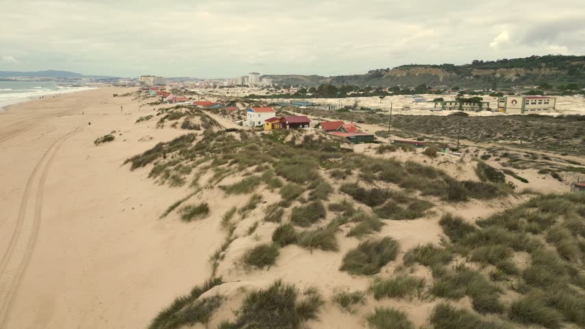 Aerial view of Praia da Mata beach with sand dunes and small coastal houses in Costa da Caparica, Setubal, Portugal.