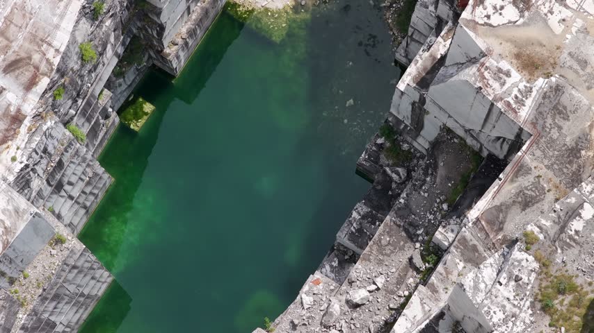 Aerial view of the turquoise water and white marble rock faces of the Carrara marble quarry in Carrara, Tuscany, Italy.