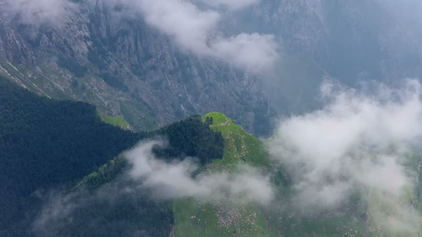 Aerial view of the rugged Apuan Alps mountains near Carrara, featuring steep rocky slopes, lush green forests, and drifting clouds in Carrara, Tuscany, Italy.