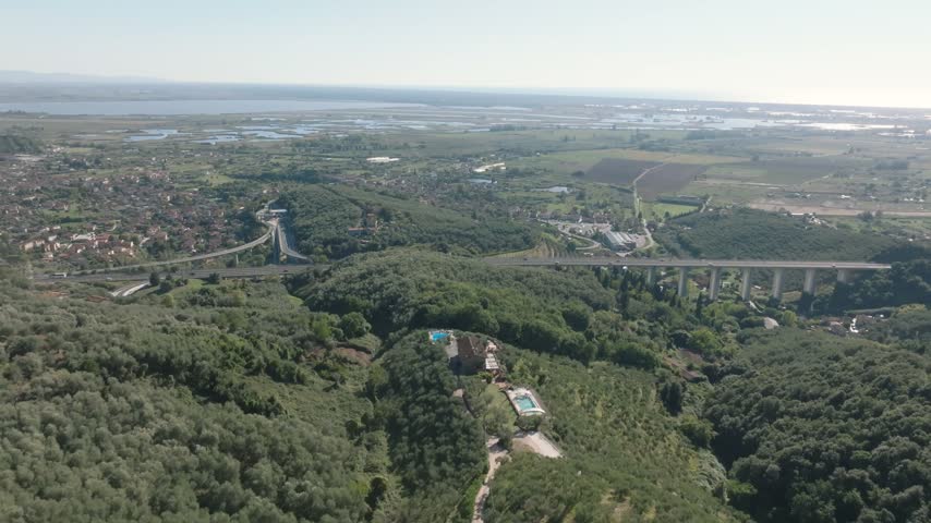 Aerial view of Chiesa di San Pantaleone in Pieve a Elici surrounded by lush hills and olive groves near the highway bridge in Massarosa, Toscana, Italy.