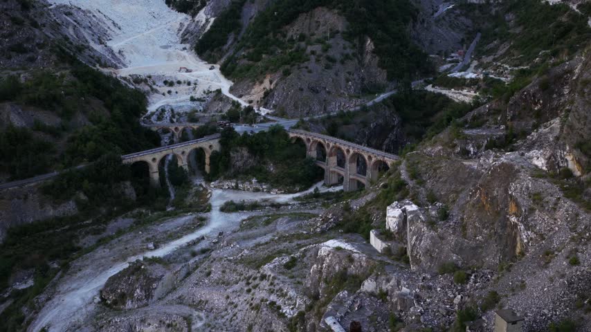 Aerial view of the historic stone railway bridge spanning the rugged marble quarries of Carrara, Tuscany, Italy.